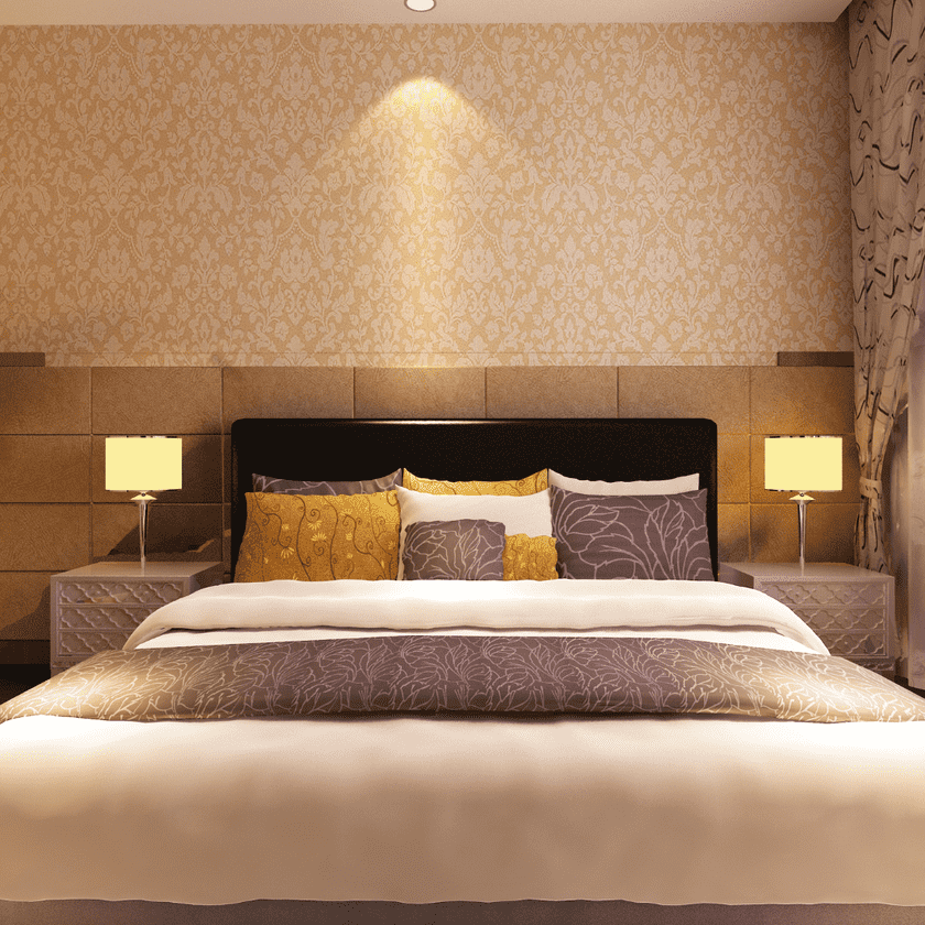 A cozy bedroom featuring a large bed with decorative pillows, a patterned headboard, and soft lighting. There are bedside lamps and a stylish wall design.