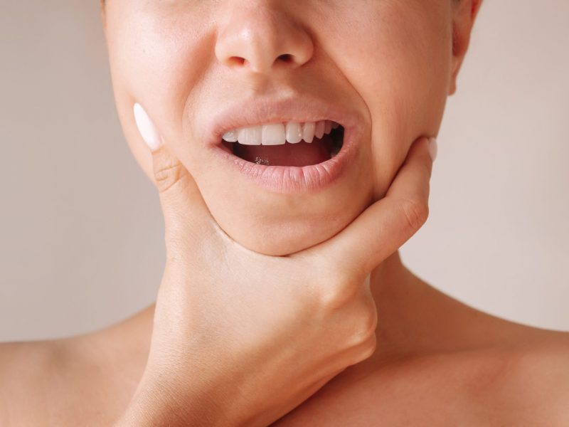 Cropped shot of a young woman suffering from jaw pain holding he